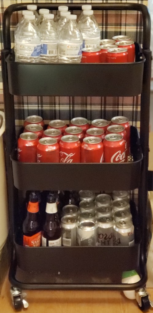 A 3 tiered black cart filled with sodas, water, and beer